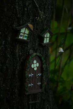 A tiny door and two miniature houses fixed to the bark of a tree.