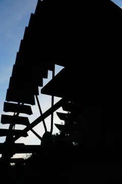 Silhouette of the wooden water wheel against a pale blue evening sky.