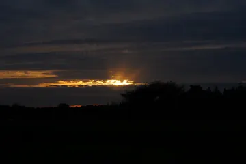 The last orange light of sunset beneath heavy, dark clouds.