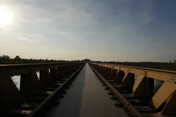 The long, straight railway bridge runs to the horizon, with the sun low on the left.