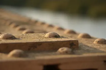 Rivets on the edge of the bridge, with blurred water beyond.