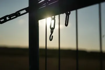A chain on the paddock gate with the low sun behind it.