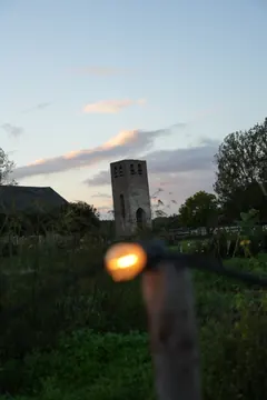 The old brick tower stands in a garden at dusk, with a warm, blurred light in the foreground.