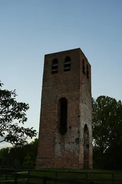 The solitary old brick tower stands against a pale blue evening sky, framed by dark trees and a fence.